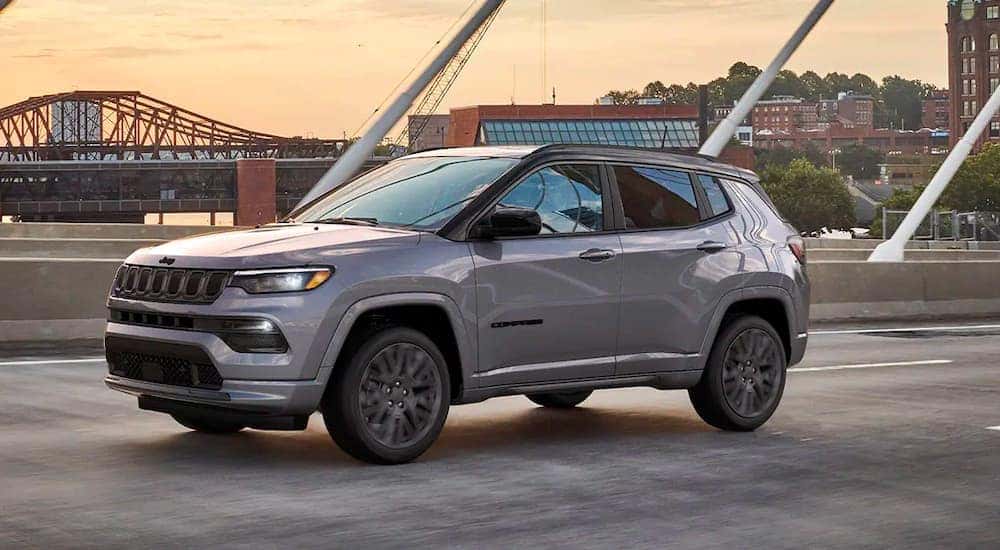 A grey 2022 Jeep Compass is shown driving over a city in a bridge.