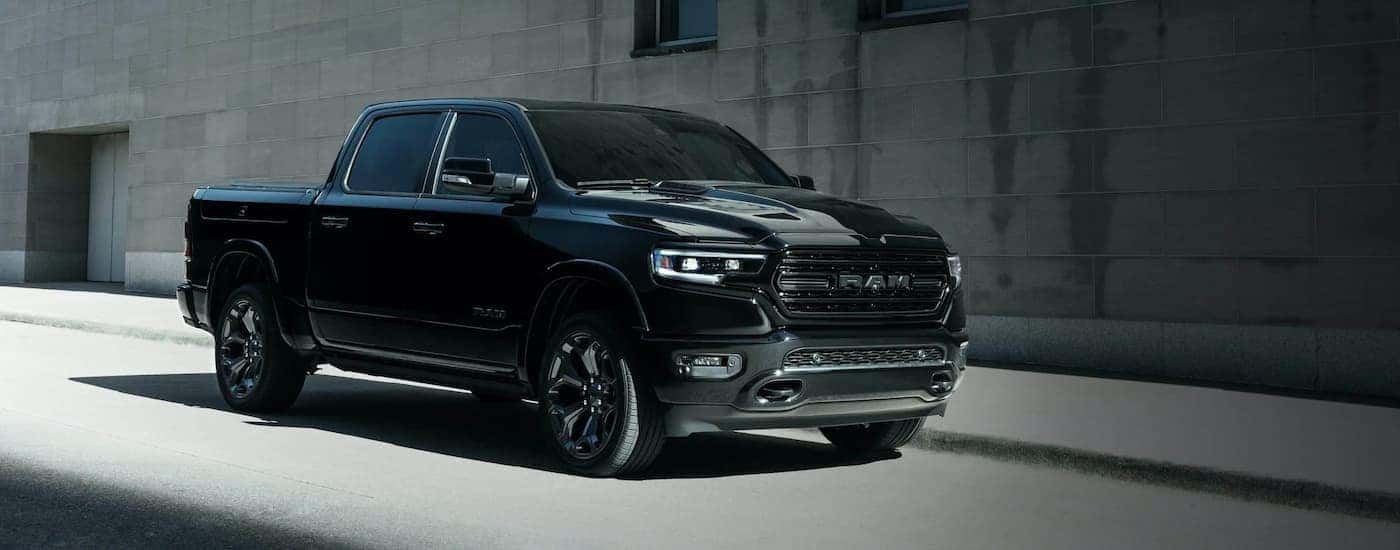 A black 2021 Ram 1500 Night Edition is shown parked in front of a concrete wall before a Ram service…