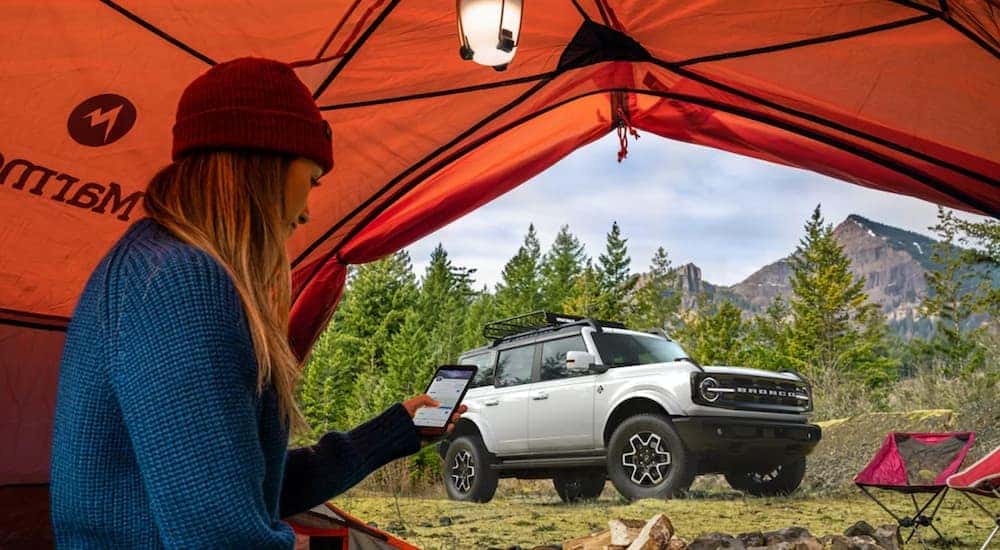 A silver 2021 Ford Bronco Outer Banks is shown parked outside of an orange tent.