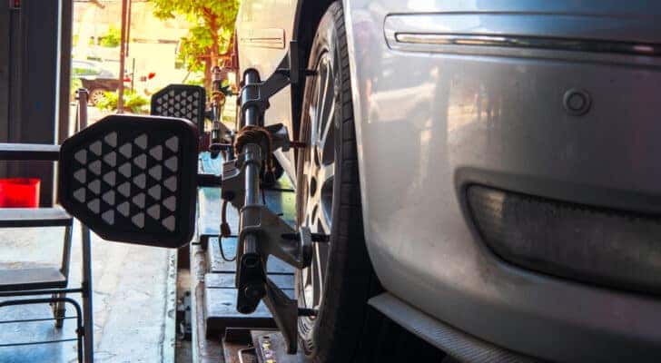 A grey car is shown getting four-wheel alignment done at a tire shop.