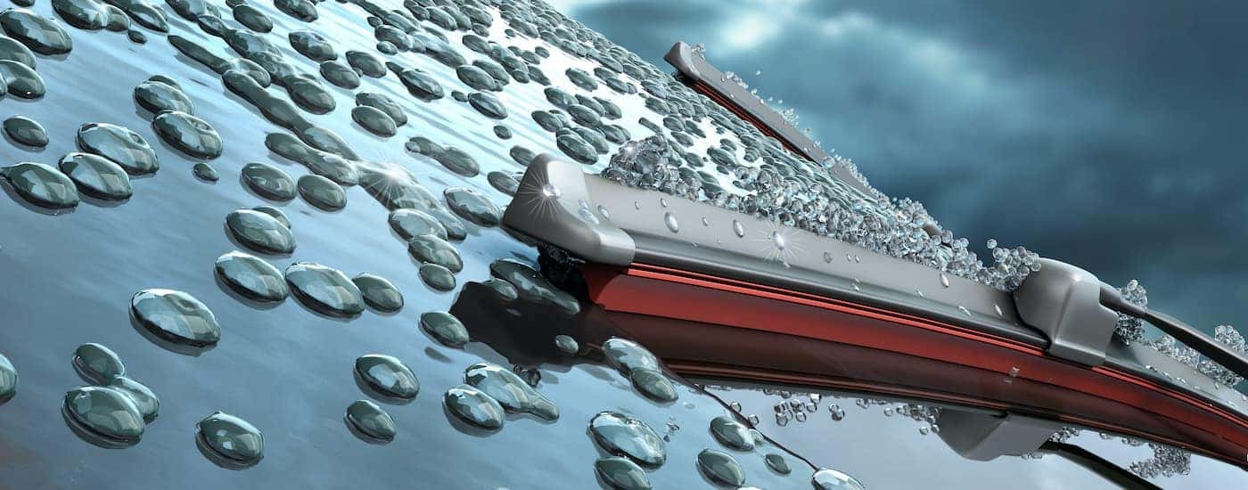 A close up shows a windshield wiper blade and rain on a windshield.