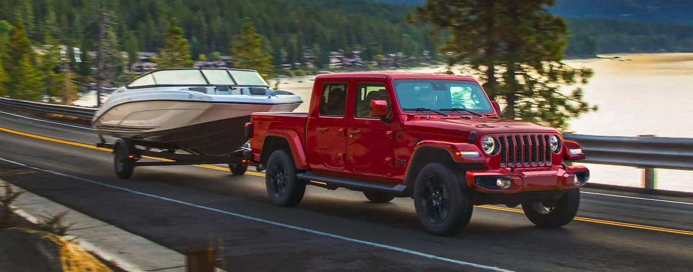 A red 2021 Jeep Gladiator is shown towing a boat past a lake.