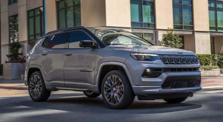 A silver 2022 Jeep Compass is shown driving through a city after researching 'Jeep service near me.'