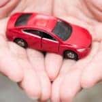 A pair of hands are shown holding a red toy car after searching 'sell my car.'