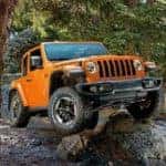 An orange 2019 Jeep Wrangler Rubicon is shown from the front at an angle while it crawls over rocks after the owner searched 'Jeep Wrangler tires'.