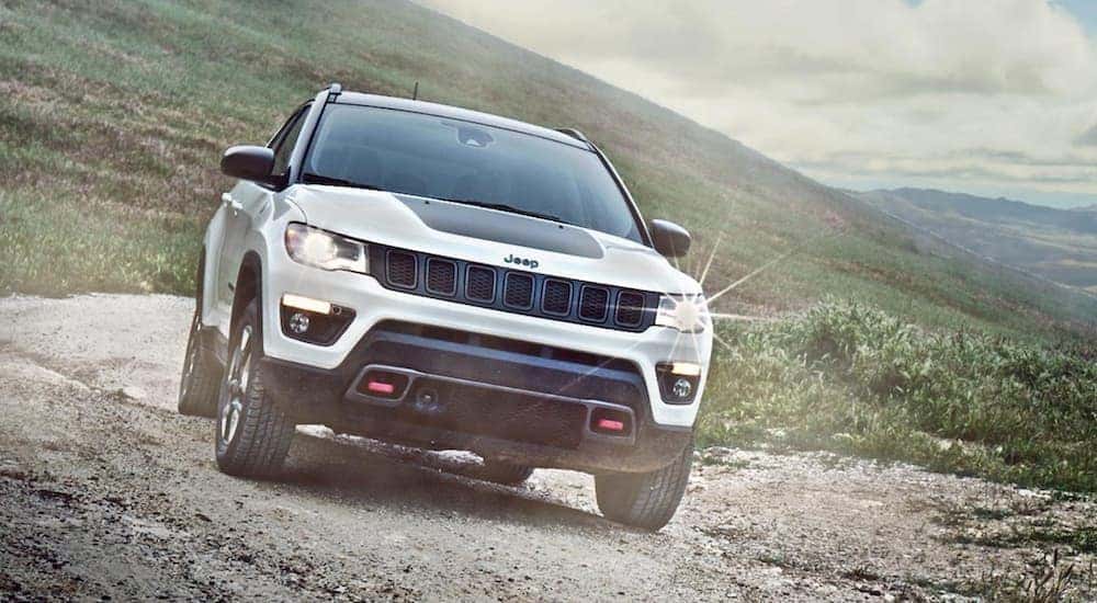 A white 2020 Jeep Compass Trailhawk is shown from the front while it drives down a trail.
