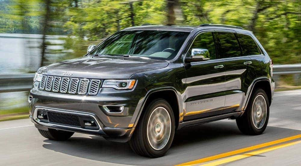 A grey 2020 Jeep Grand Cherokee is shown from the front at an angle while driving down the road.