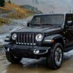 A black 2018 Jeep Wrangler Unlimited is shown from the front off-roading on a muddy trail.