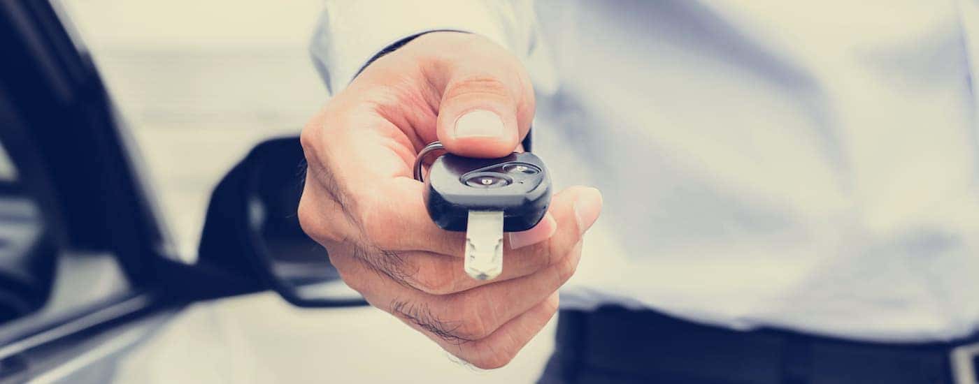 A person is shown holding out a car key.