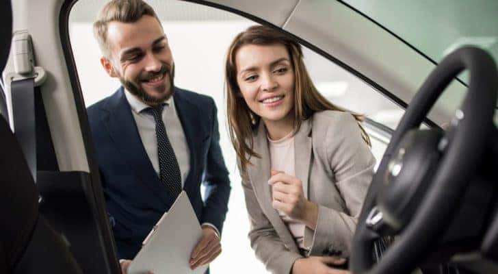 A person is shown looking into a vehicle with a salesperson.