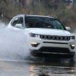 A white 2021 Jeep Compass is shown driving through a puddle.