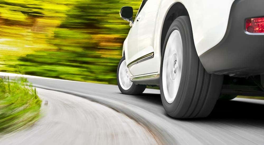 A close up of the side of a white SUV is shown speeding on a winding road.