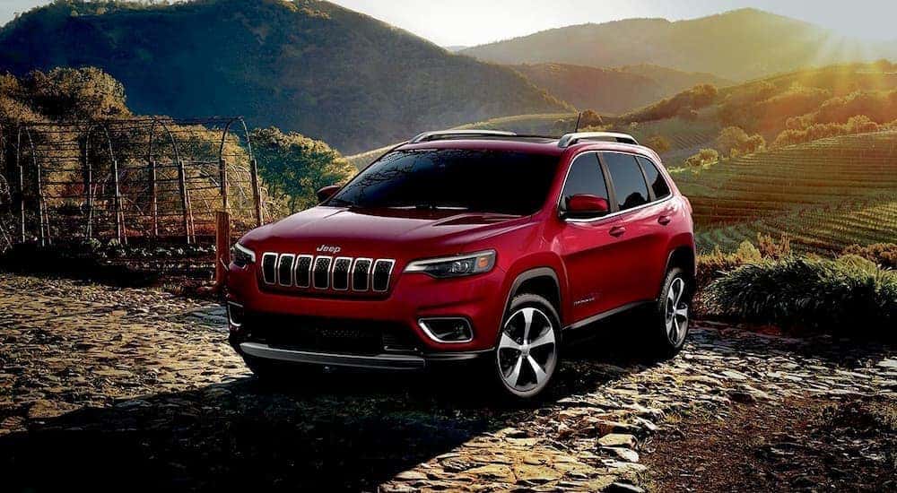 A popular used Jeep Cherokee for sale in Colorado, a red 2019 Jeep Cherokee, is shown parked in the mountains.