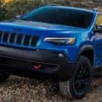 A blue 2019 Jeep Cherokee Trailhawk is shown driving on a dirt trail.