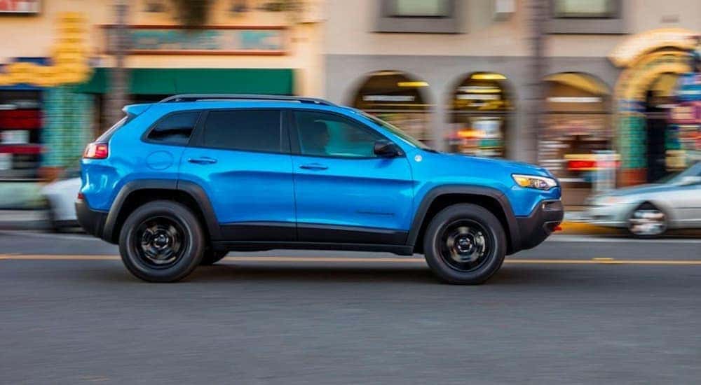 A blue 2020 Jeep Cherokee Trailhawk is shown from the side driving in a city.