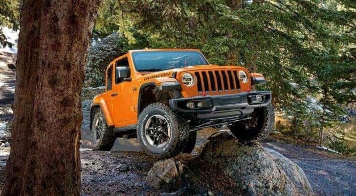 An orange 2019 Jeep Wrangler is shown from the front at an angle while driving over a rock.