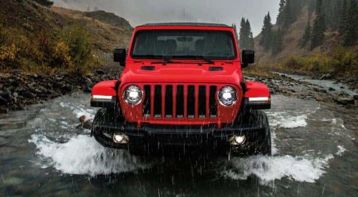 A red 2022 Jeep Wrangler Rubicon is shown from the front while fording through a river.
