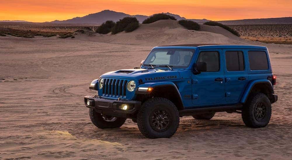 A blue 2022 Jeep Wrangler Rubicon 392 is shown parked in a desert during a sunset.