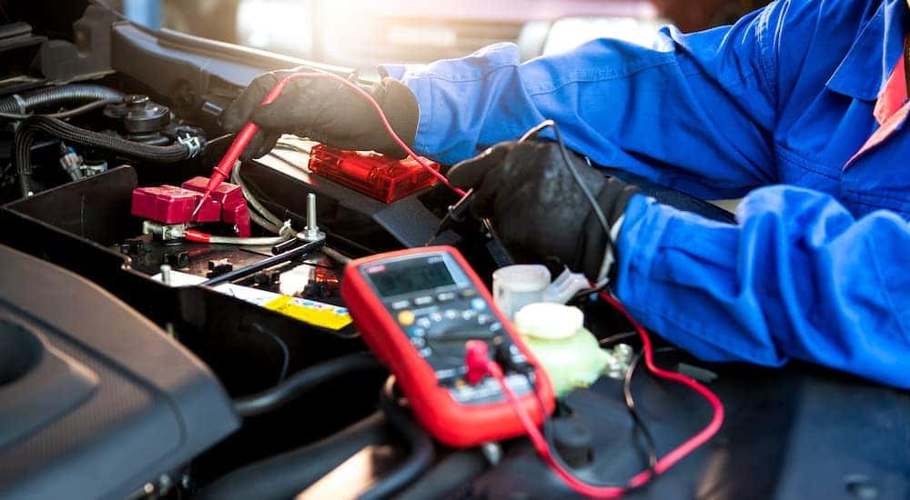 A mechanic is shown checking a car's battery with a multimeter.