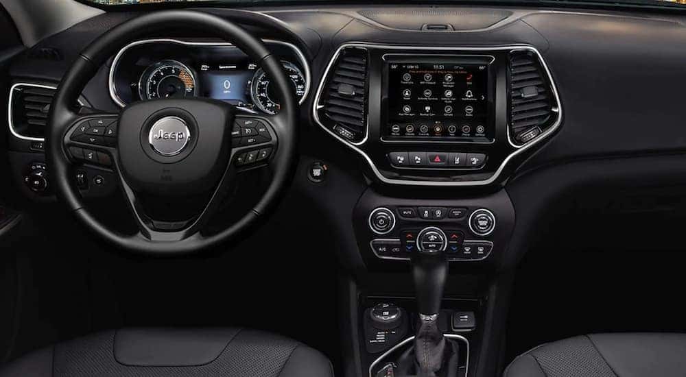 The black interior of a 2023 Jeep Cherokee shows the steering wheel and infotainment screen.