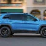 A blue 2023 Jeep Cherokee is shown from the side driving through a city.