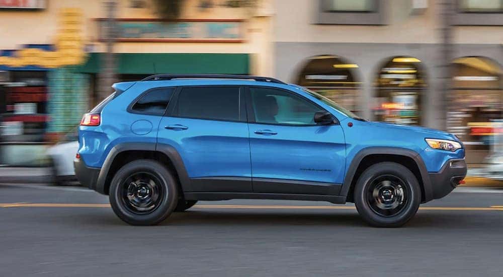 A blue 2023 Jeep Cherokee is shown from the side driving through a city.