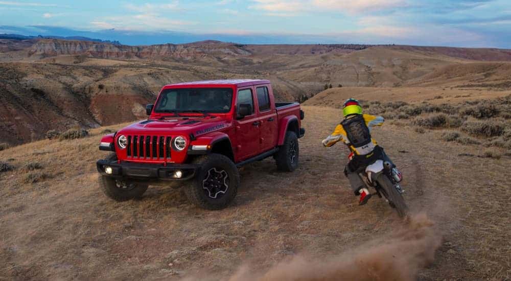 A red 2023 Jeep Gladiator Rubicon is shown from the front next to a dirt bike.