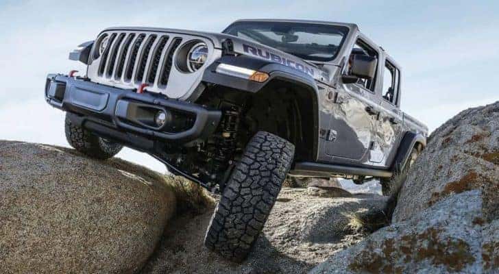 A silver 2023 Jeep Gladiator Rubicon for sale is shown off-roading on a rocking trail.