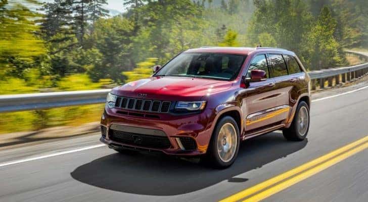 A red 2018 used Jeep Grand Cherokee for sale in Colorado Springs is shown driving on an open road.