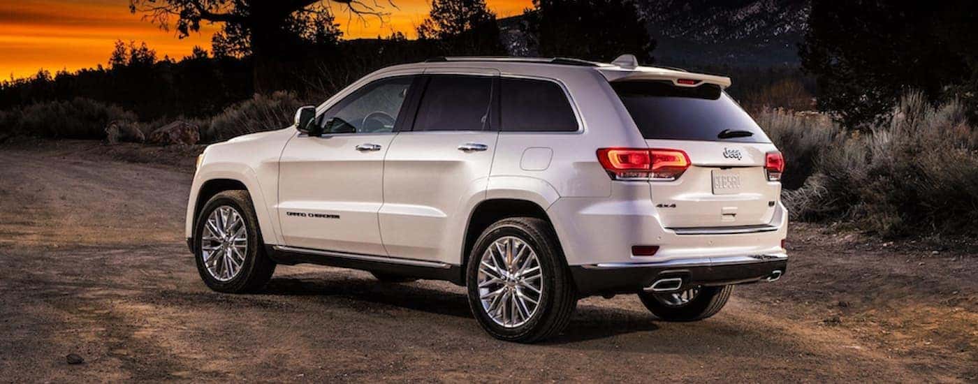 A white 2018 Jeep Grand Cherokee is shown from a rear angle parked on a dirt road.