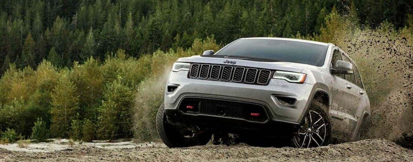 A silver 2019 Jeep Grand Cherokee Trailhawk is shown off-roading on a muddy trail.