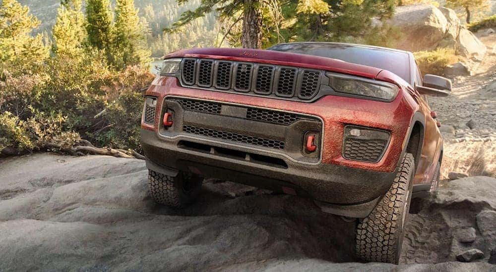 A red 2022 Jeep Grand Cherokee TrailHawk is shown from the front at an angle while climbing a hill.