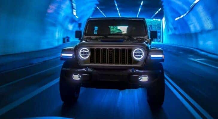 A gray 2024 Jeep Wrangler is shown driving in a dark tunnel after having a headlight replacement.