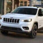 A white 2023 Jeep Cherokee Altitude LUX is shown driving on a city street.
