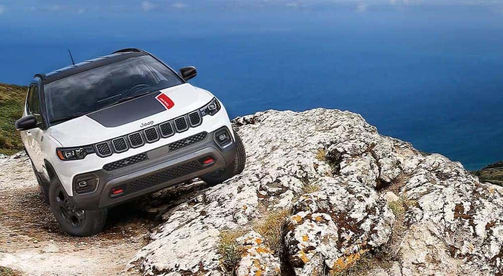 A white 2023 Jeep Compass Trailhawk is shown off-roading with an ocean view.