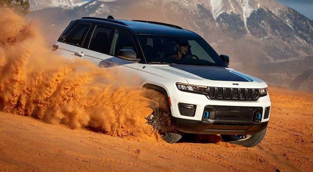 A white 2024 Jeep Grand Cherokee 4xe is shown driving off-road down a sandy dune.