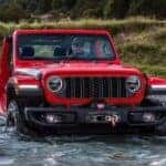 A red 2024 Jeep Wrangler Rubicon is shown fording a shallow river.
