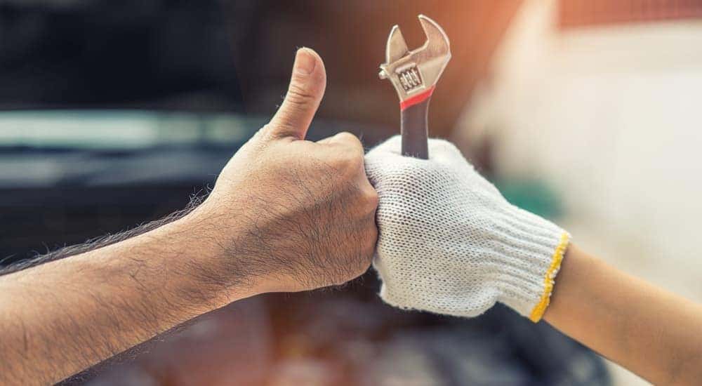 A hand is shown with a thumbs up while posed next to a gloved hand holding a wrench.