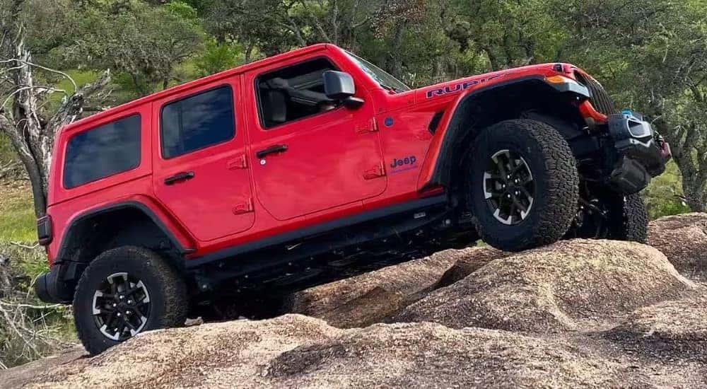 A red 2024 Jeep Wrangler 4xe Rubicon for sale near Monument, CO is shown driving up a rocky hill.