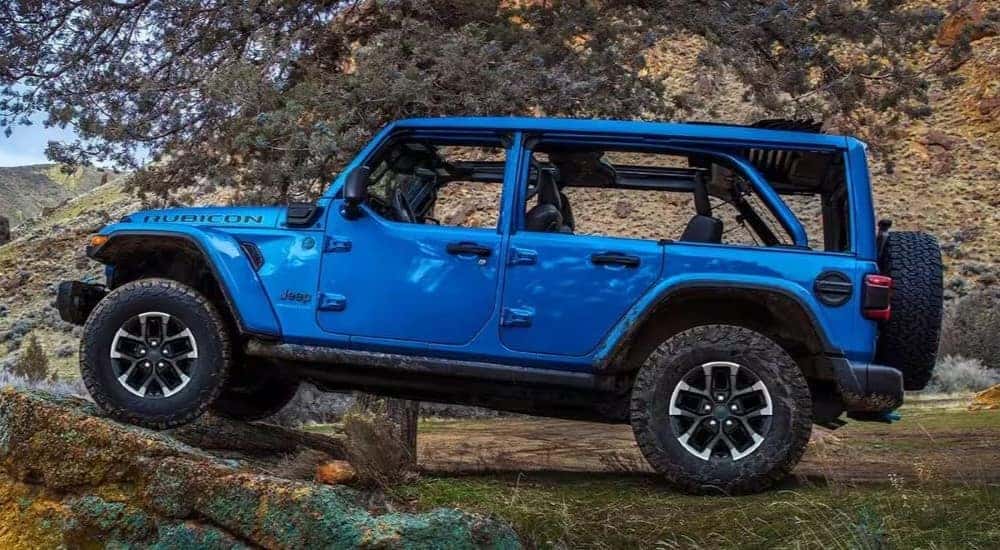 A blue 2024 Jeep Wrangler 4xe Rubicon is shown at a side angle while driving off-road.
