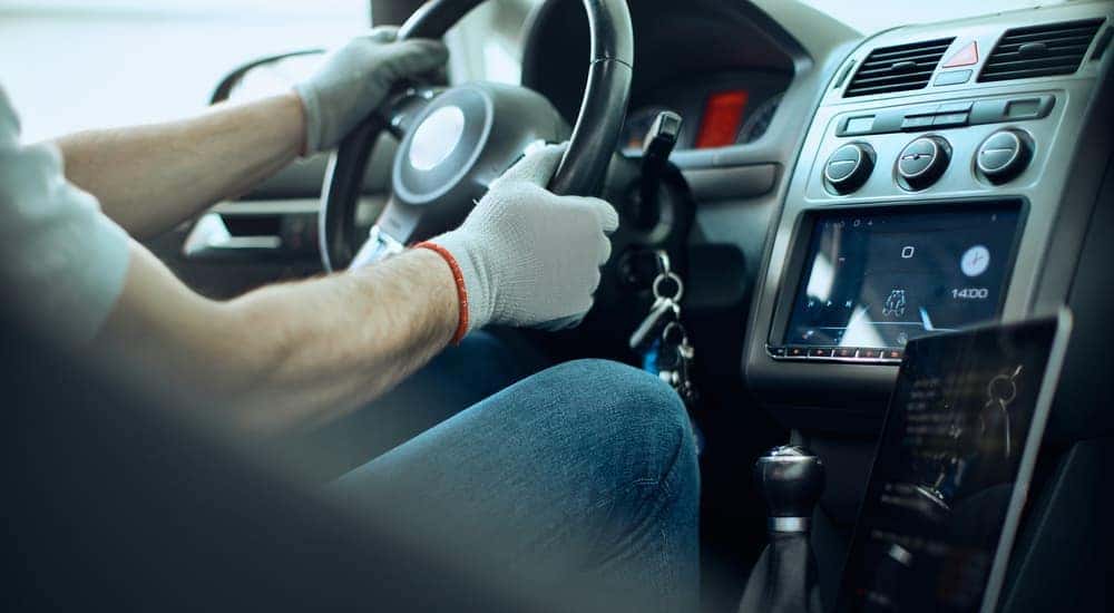 A mechanic is shown sitting in the driver's seat of a car and holding the steering wheel.