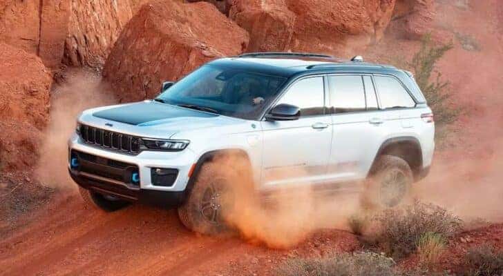 A white 2024 Jeep Grand Cherokee 4xe is shown driving off-road after viewing electric vehicles for sale.