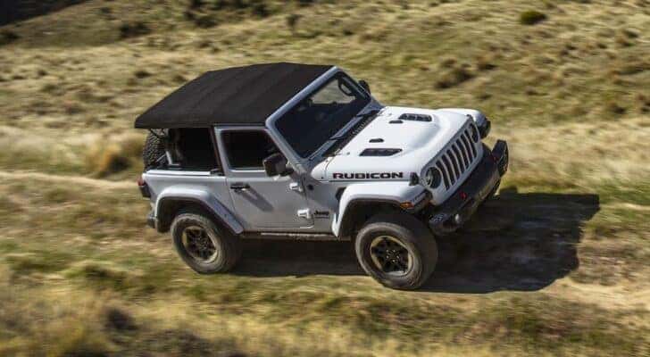 A white 2019 Jeep Wrangler Rubicon is driving through a field.