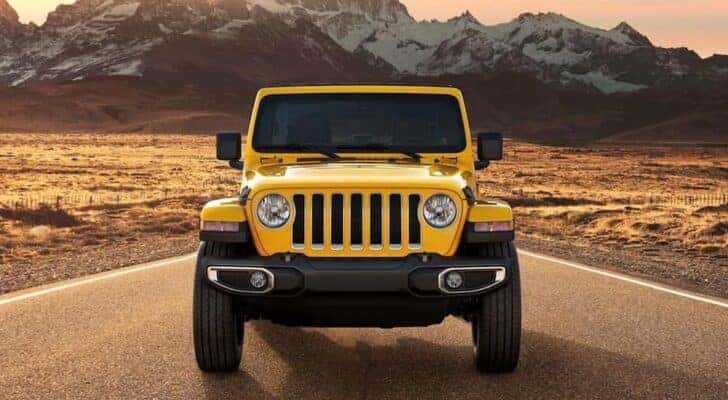 Head-on view of a yellow 2021 Jeep Wrangler parked in front of mountains.