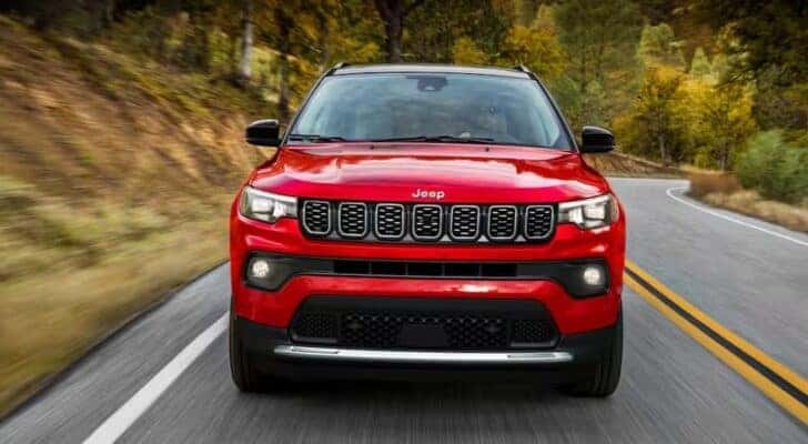 A red 2025 Jeep Compass for sale is shown driving on a highway.