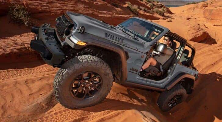 A gray 2025 Jeep Wrangler Willys is shown off-roading.