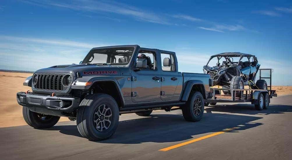 A gray 2025 Jeep Gladiator Mojave is shown towing a trailer on a highway.