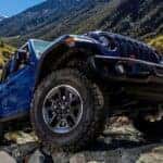 Low-angle view of a blue 2019 Jeep Wrangler Rubicon driving off-road from a dealer with a used cars for sale in Colorado Springs.