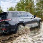 Black 2025 Jeep Grand Cherokee off-roading in a river.