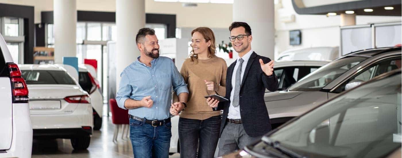 A couple speaking to a salesman about used vehicles.